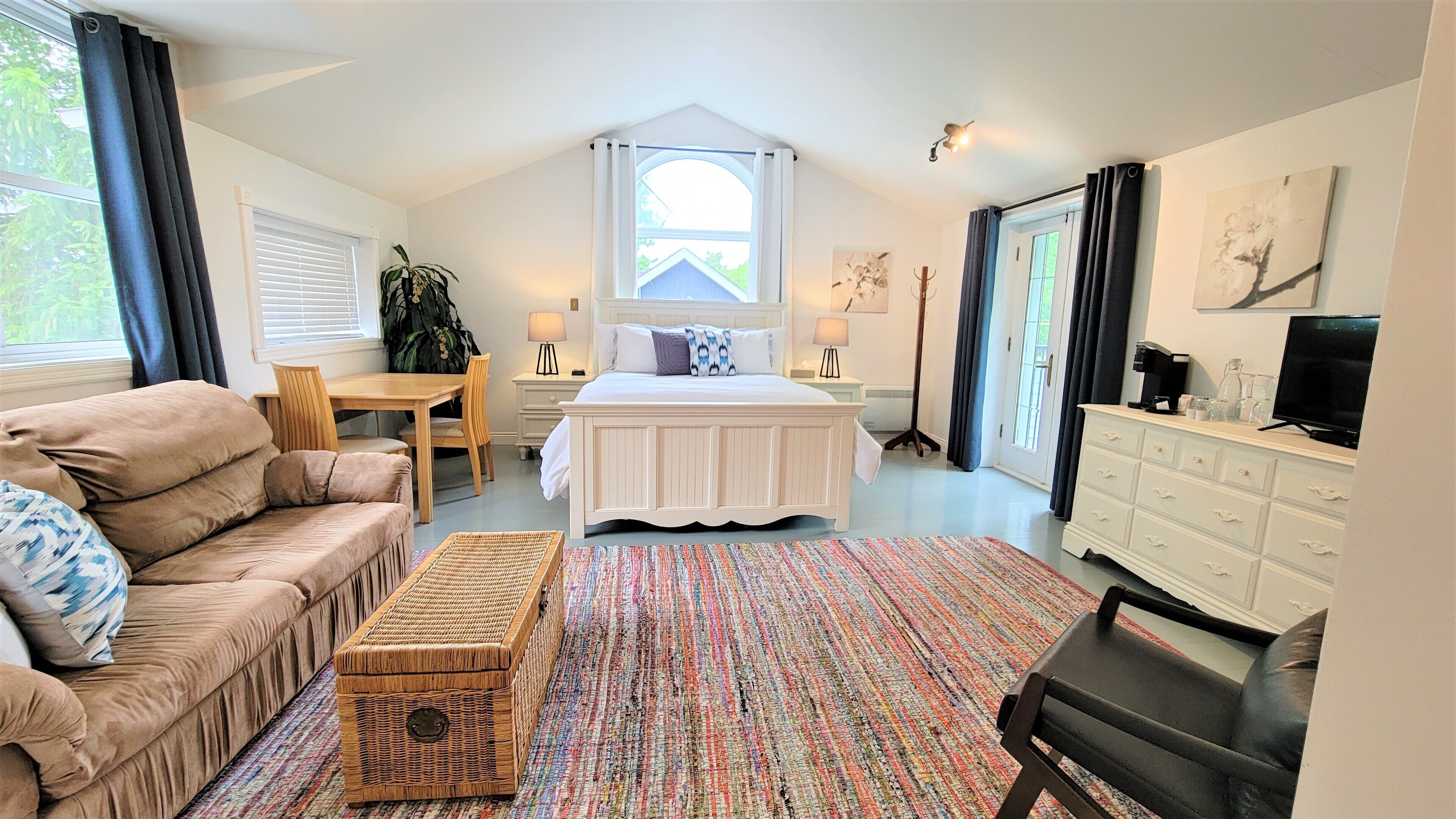 A bedroom with a bed, a sofa, a dining table, a TV, and a dresser.