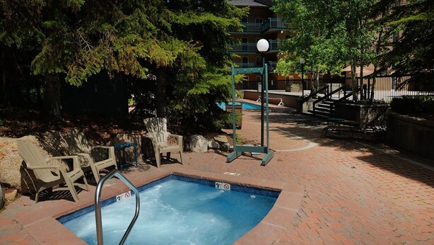 A small outdoor swimming pool with a metal ladder, surrounded by brick flooring and wooden chairs. - Vantage Point Condo 303 (Vail)