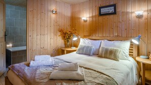 A wooden-paneled room with a bed, two bedside tables, a wall-mounted picture, and a vase with flowers.