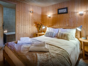 Una habitación con paneles de madera, una cama, dos mesitas de noche, un cuadro colgado en la pared y un florero con flores.