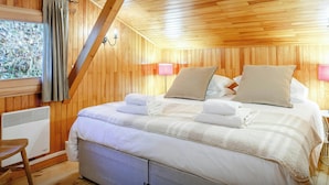 A wooden-paneled room with a bed, pillows, a heater, and a window with curtains. - Chalet Bellanis - ski holiday for 10 in the heart of Morzine - OVO Network (Morzine)