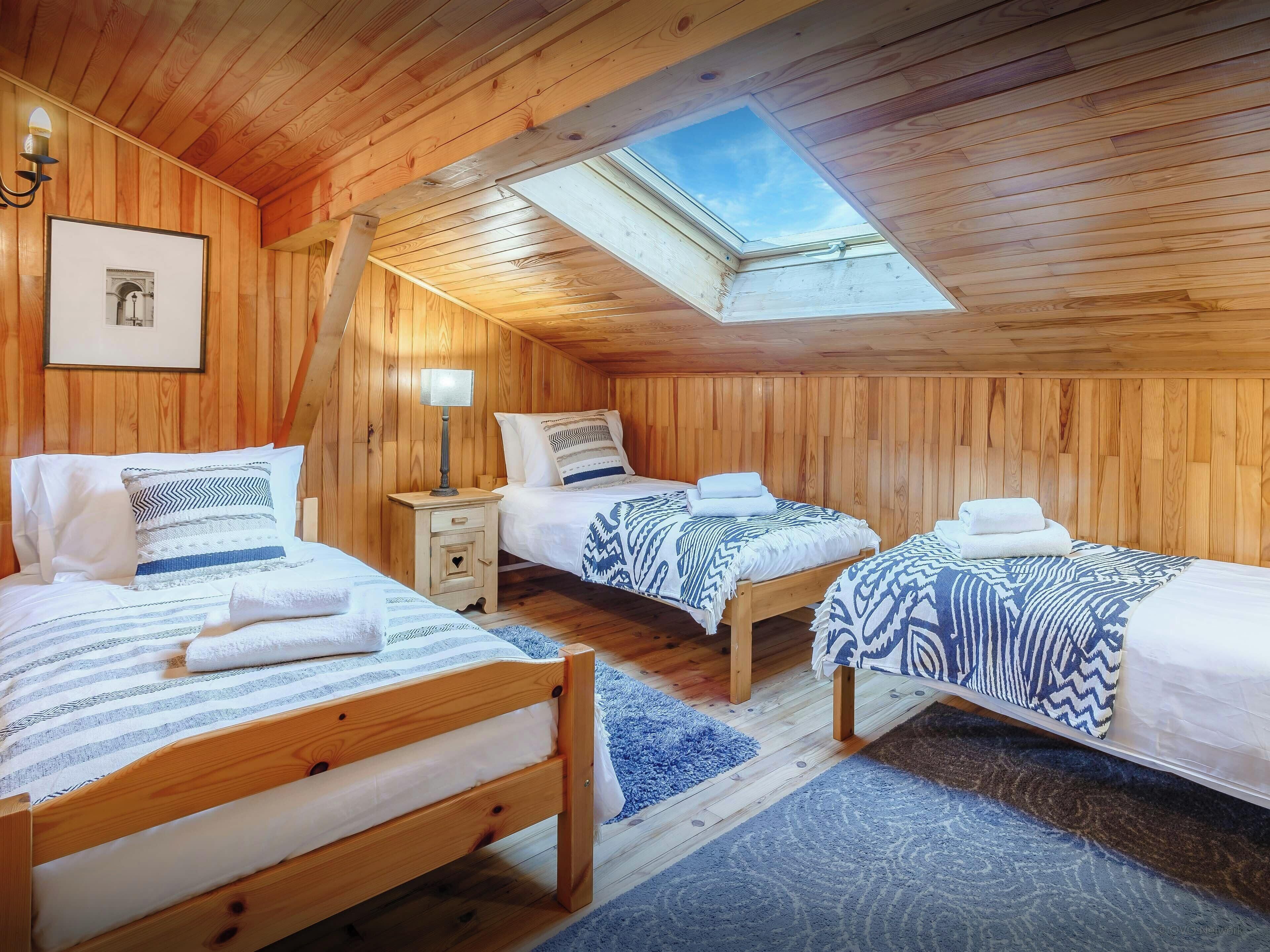 Un dormitorio acogedor tipo cabaña de madera con tres camas, un tragaluz y un cuadro en la pared.