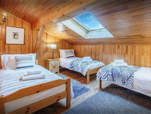 Une chambre confortable, aménagée dans un chalet en bois, avec trois lits, une lucarne et un tableau encadré au mur.