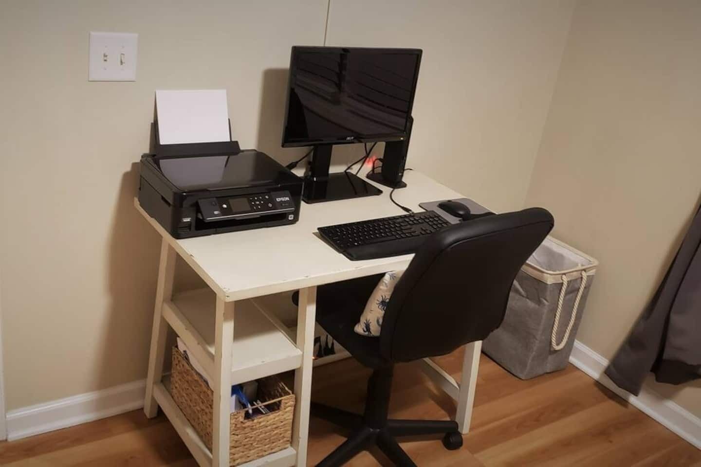 Ein kompakter Arbeitsplatz mit Drucker, zwei Monitoren, Tastatur und Stuhl.