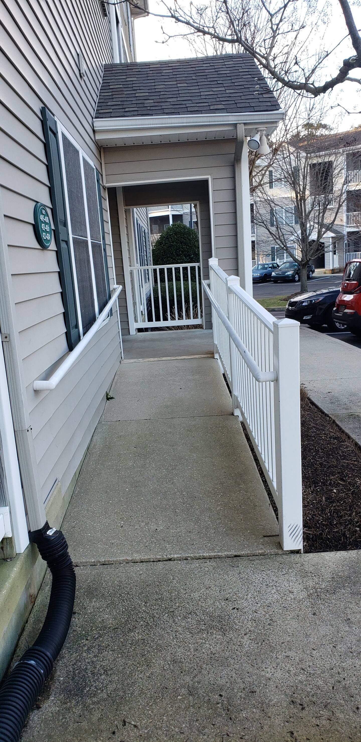A residential building with a covered entryway, a white railing, and a driveway leading to parked cars.