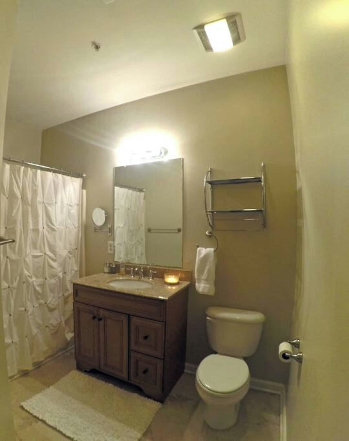 Un baño con cortina de ducha, un lavabo con espejo, un inodoro y un perchero para toallas.
