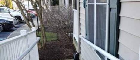 A narrow concrete pathway leading to a building with white siding and a white fence on one side.