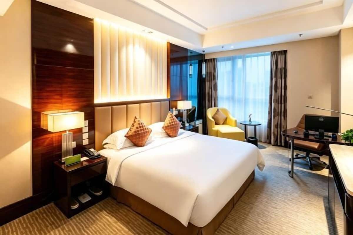 Una habitación de hotel con una cama grande, mesitas de noche, un escritorio y un televisor.