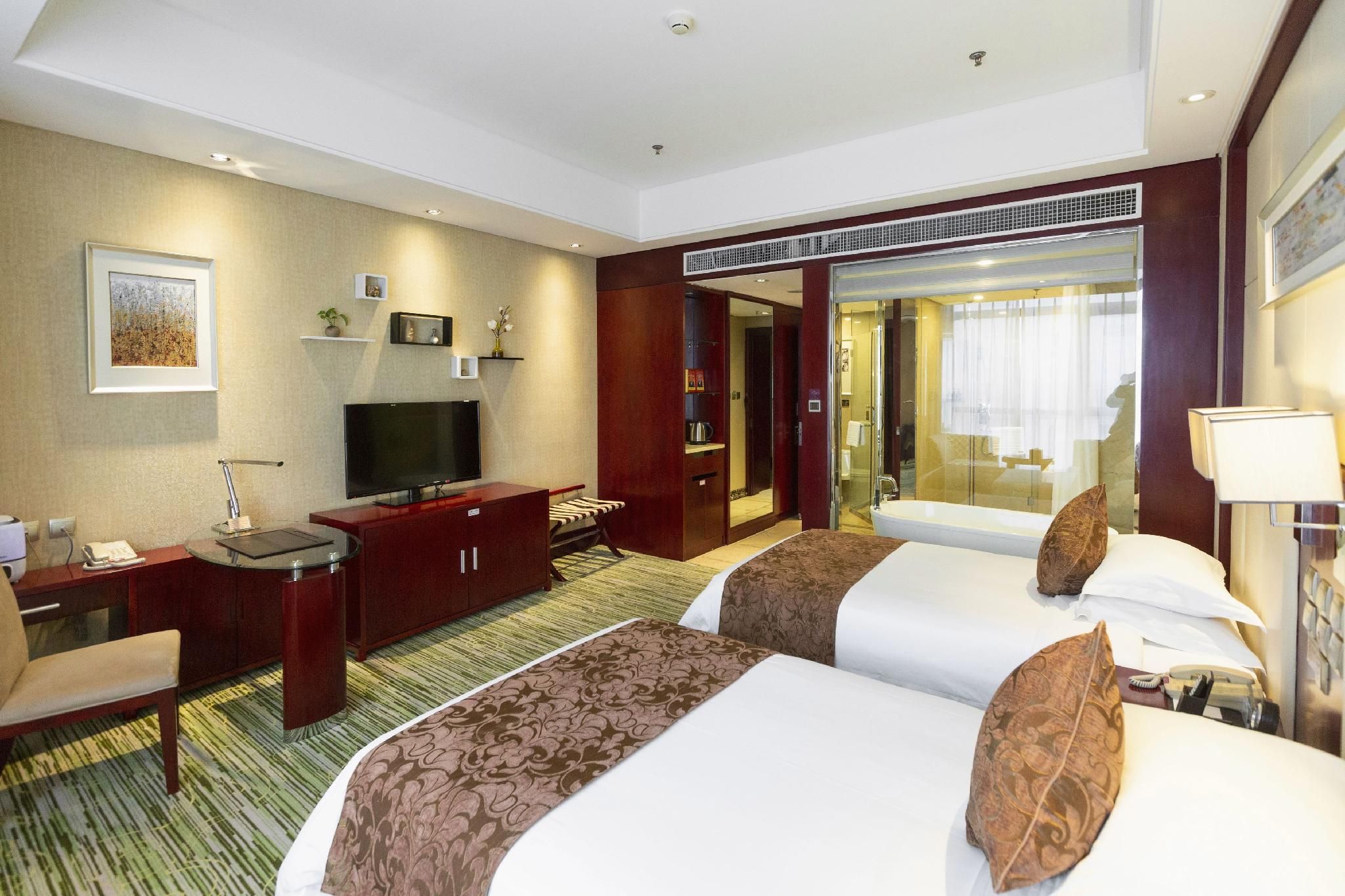 A hotel room with a bed, a desk, a television, a wardrobe, and a bathroom visible through an open door.