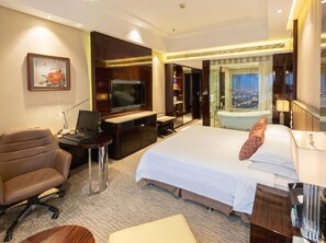 Ein Hotelzimmer mit Bett, Schreibtisch, Stuhl, Fernseher und Blick auf die Stadt.