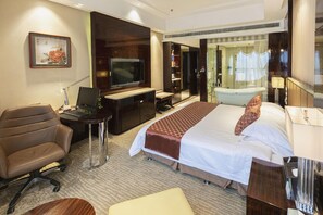 Une chambre d’hôtel comprenant un lit, un bureau, une chaise, une télévision et une salle de bain avec une baignoire et une douche.