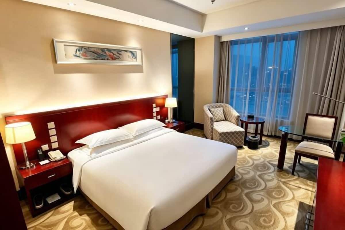 Habitación de hotel con una cama grande, mesitas de noche, una silla, un escritorio y un ventanal con cortinas.