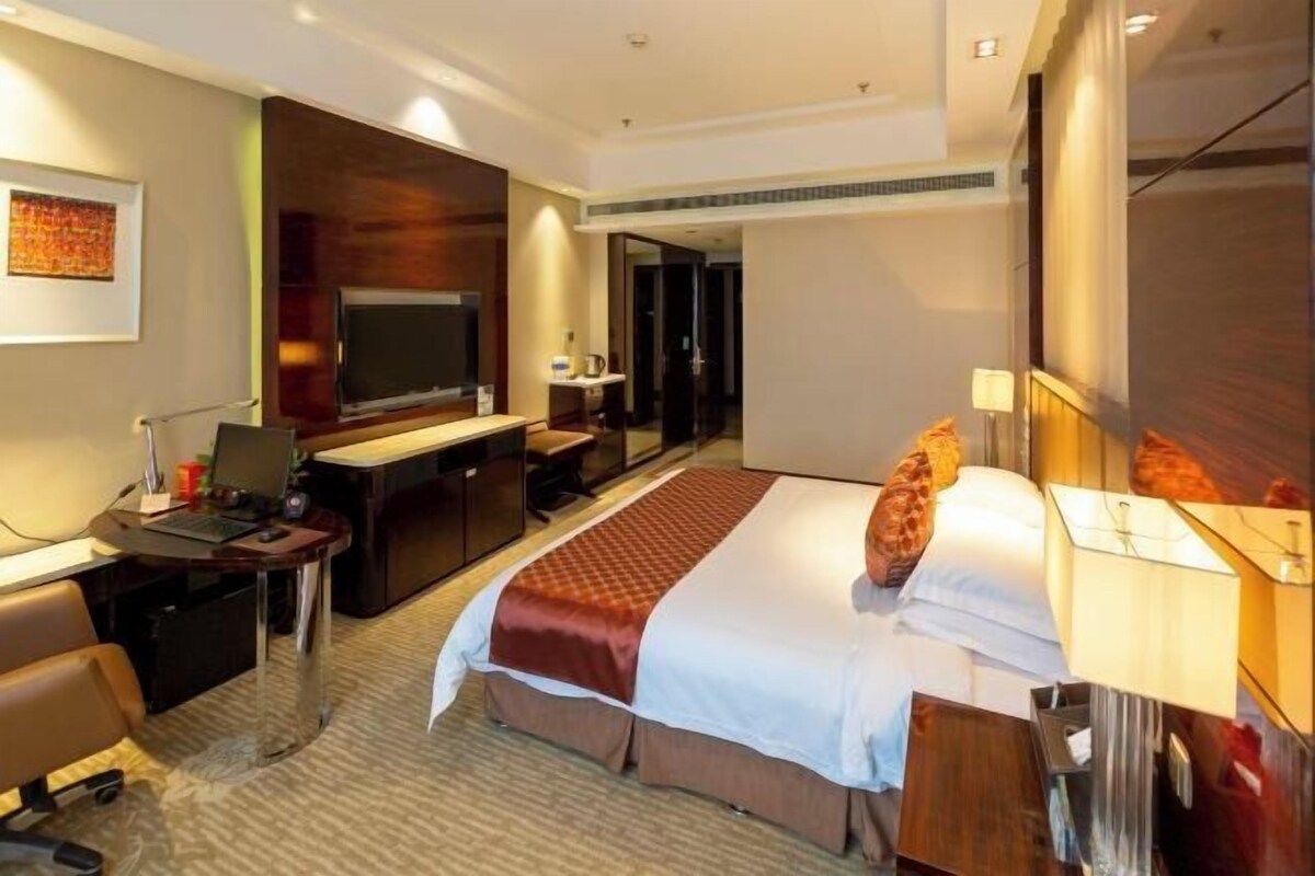 Una habitación de hotel con cama, escritorio, silla, televisor y espejo.