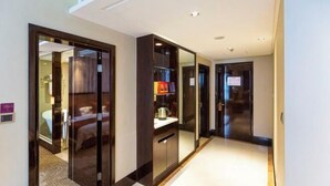 A hotel corridor with a mirrored wardrobe, a bed visible through the mirror, and a small shelf with a kettle. - Pidu International Hotel (Xinji)