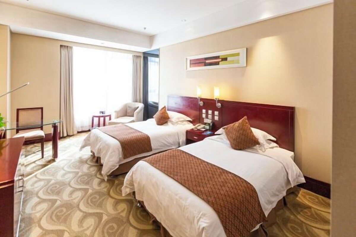 Habitación de hotel con dos camas, un escritorio, una silla y una ventana con cortinas.