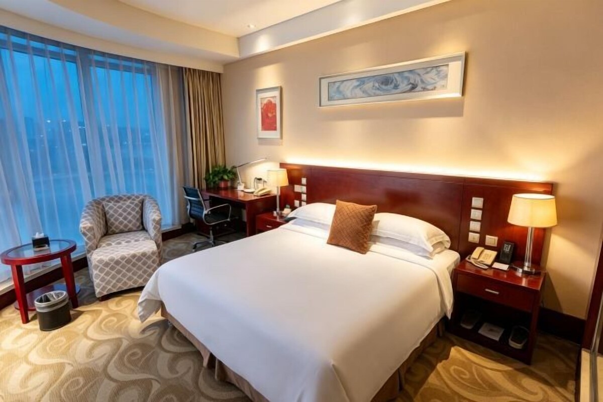 Une chambre d’hôtel avec un grand lit, un bureau, une chaise, une table de chevet et une vue sur la ville.