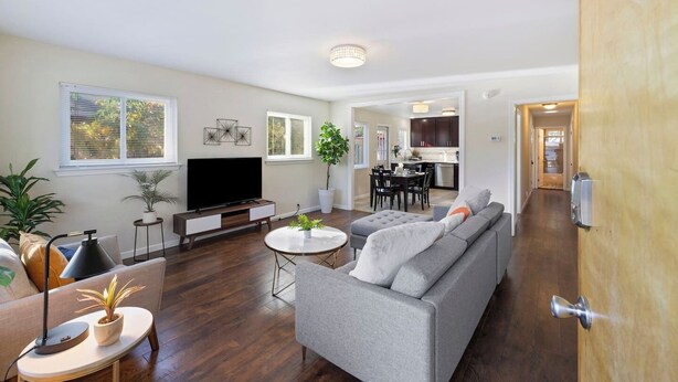 A modern living room with a flat-screen TV, grey sofa, and a dining area with a table and chairs.