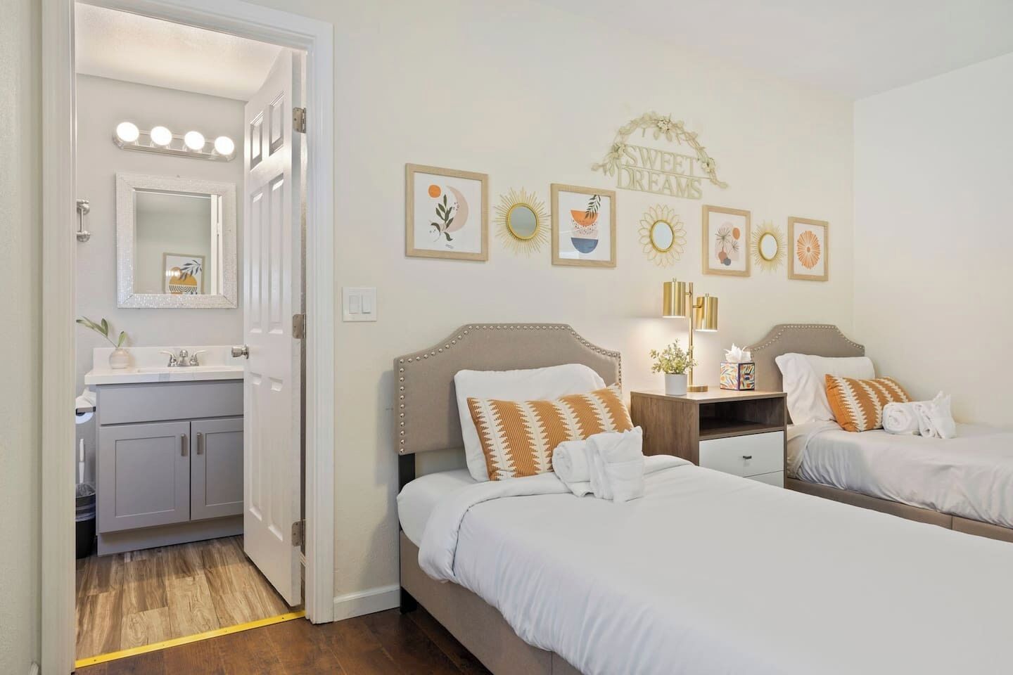 Une chambre d’hôtel avec deux lits, une coiffeuse avec un miroir et un mur décoré d’œuvres d’art encadrées.
