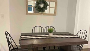 A dining room with a wooden table, black metal chairs, a bench, a mirror with a wreath, and a sign above the mirror.