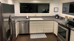 A modern kitchen with stainless steel appliances, white cabinetry, a large window, and a built-in dishwasher.