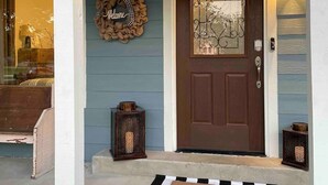 A house entrance with a brown door, a welcome mat, a lantern, and a wreath with the word "Welcome".