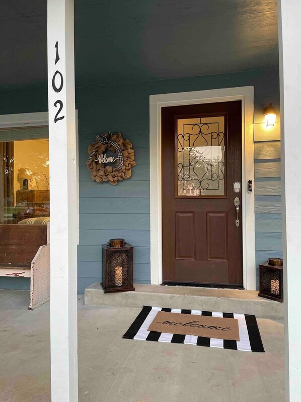 A house entrance with a brown door, a welcome mat, a lantern, and a wreath with the word "Welcome".