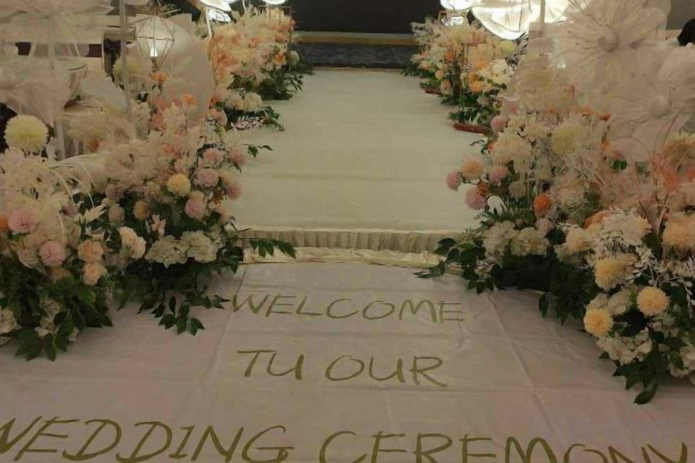 A wedding ceremony aisle with floral decorations and a welcome mat.