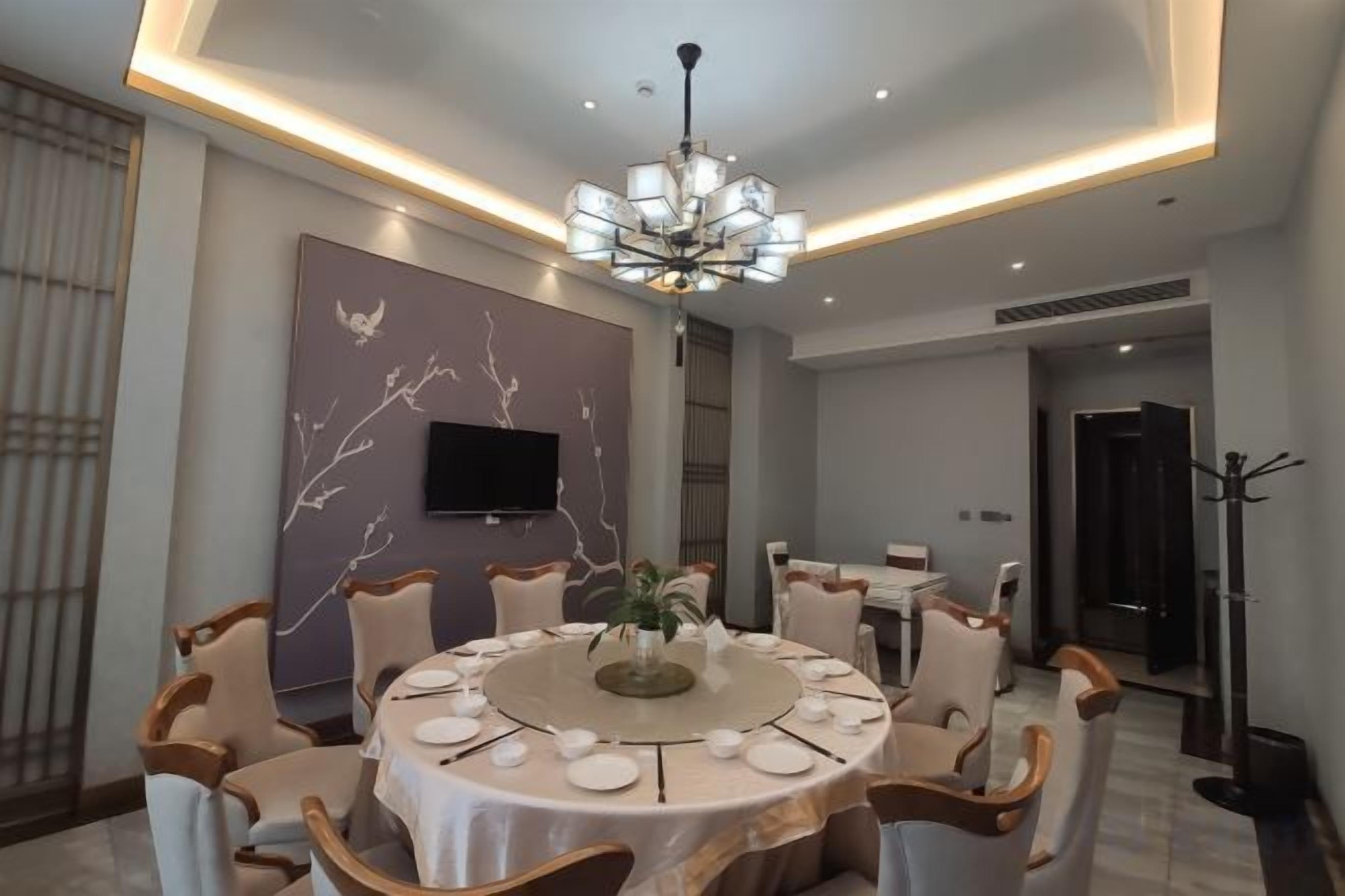 Un comedor con una mesa redonda, sillas, una araña y un televisor montado en la pared.