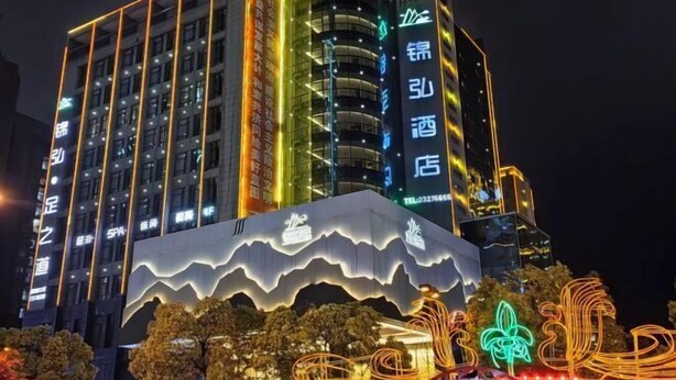 A multi-story hotel with illuminated signage and a distinctive wave-like design at the base. - Jinhong Hotel (Zheng'an)