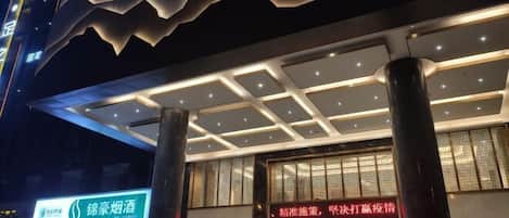 L’entrée d’un hôtel au design moderne, avec un auvent imposant et une enseigne lumineuse bien visible.