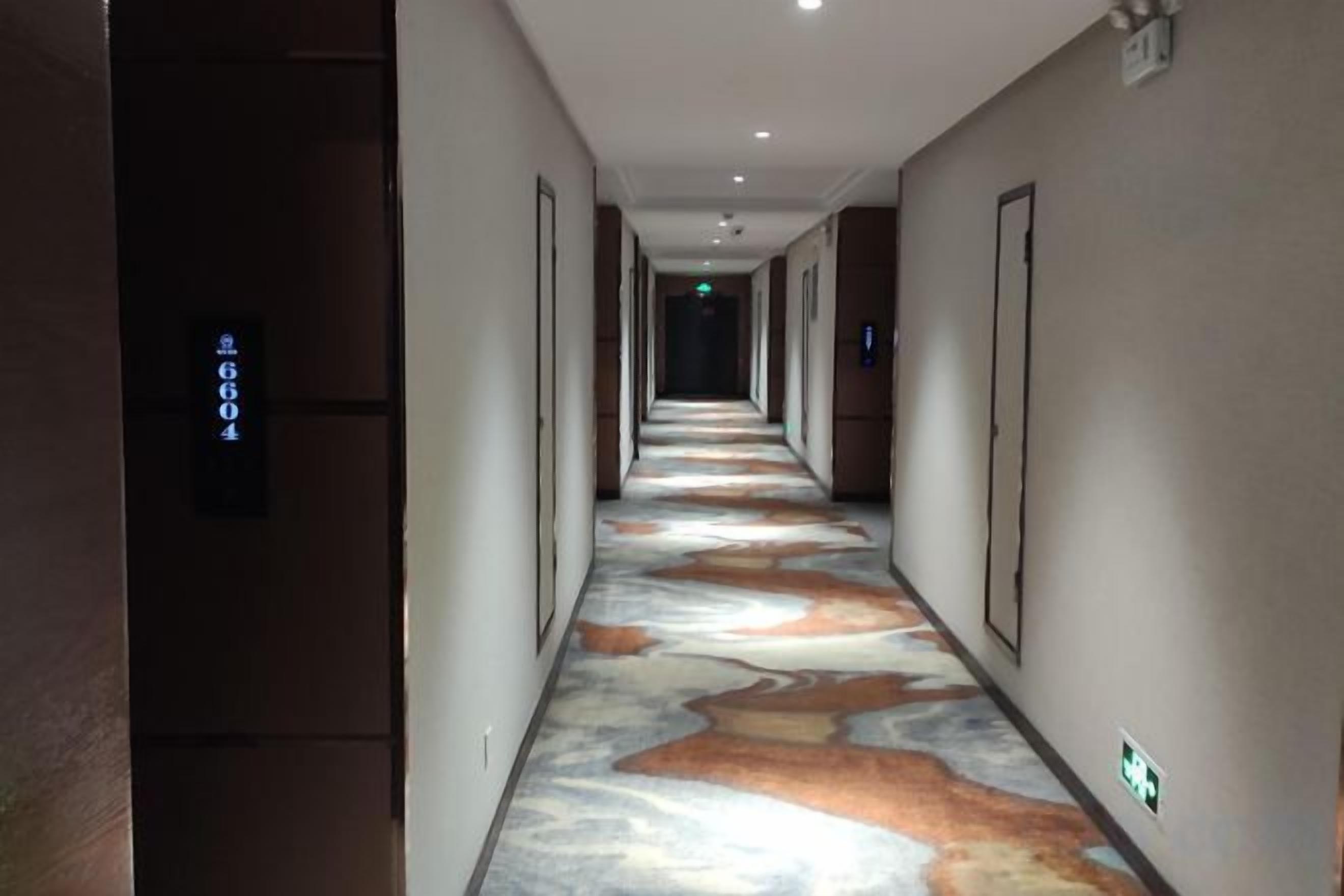 A hotel corridor with a patterned floor, doors on both sides, and a sign indicating room number 604.
