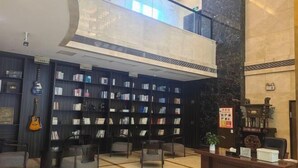 A lobby with a central reception desk, multiple seating areas, and a large bookshelf filled with books. - Jinhong Hotel (Zheng'an)