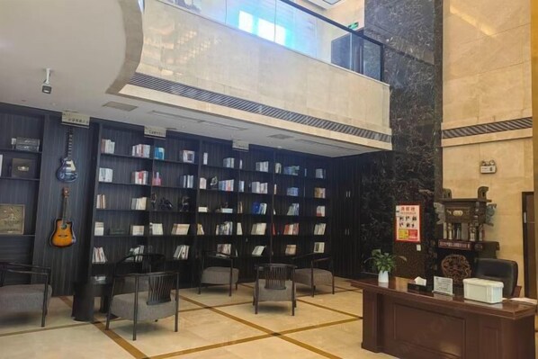 Um lobby com uma recepção central, diversas áreas de estar e uma grande estante cheia de livros.