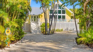 A yellow building with a white fence, surrounded by palm trees and a gravel path.
