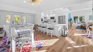 A spacious kitchen with white cabinetry, a central island, and a dining area with white chairs and a patterned rug.