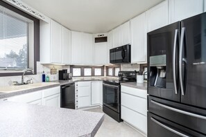 A modern kitchen with white cabinets, a black refrigerator, a microwave, and a stove.