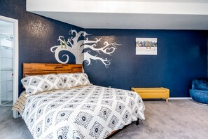 A bedroom with a bed, a wooden headboard, a blue accent wall, a small yellow side table, and a blue chair.