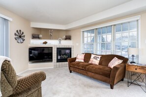 A living room with a fireplace, a large window, and a brown sofa.