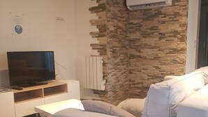 A modern living room with a flat-screen TV on a white console, a stone accent wall, and a white sofa. - Joli studio les brimbelles (Granges-Aumontzey)