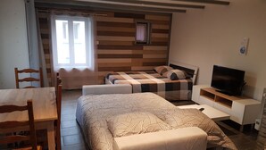A compact bedroom with a bed, bedside table, TV, and a window with curtains. - Joli studio les brimbelles (Granges-Aumontzey)
