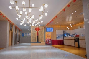 Un vestíbulo de hotel con una recepción, una pantalla de televisión y una cortina roja.