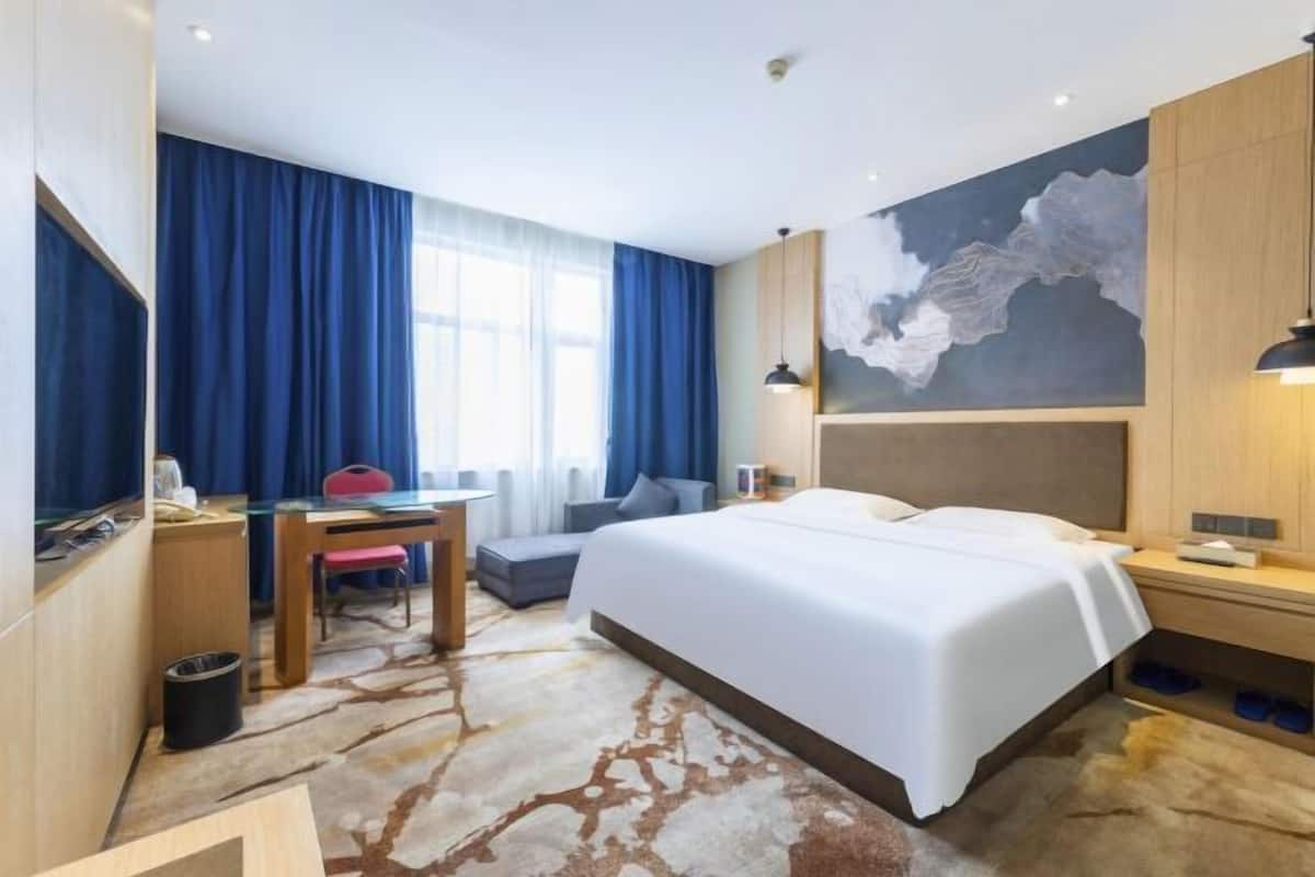A hotel room with a large bed, a desk, a chair, a map on the wall, and a window with curtains.