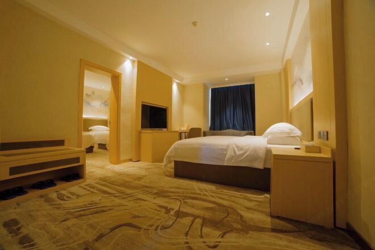 A hotel room with a bed, bedside table, TV, and a desk with a chair.
