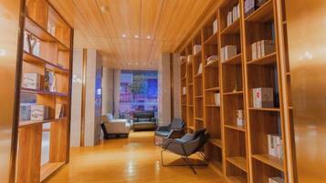 Un couloir avec des étagères en bois, un coin salon avec des fauteuils, et une vue sur une pièce où se trouvent un canapé et une table.