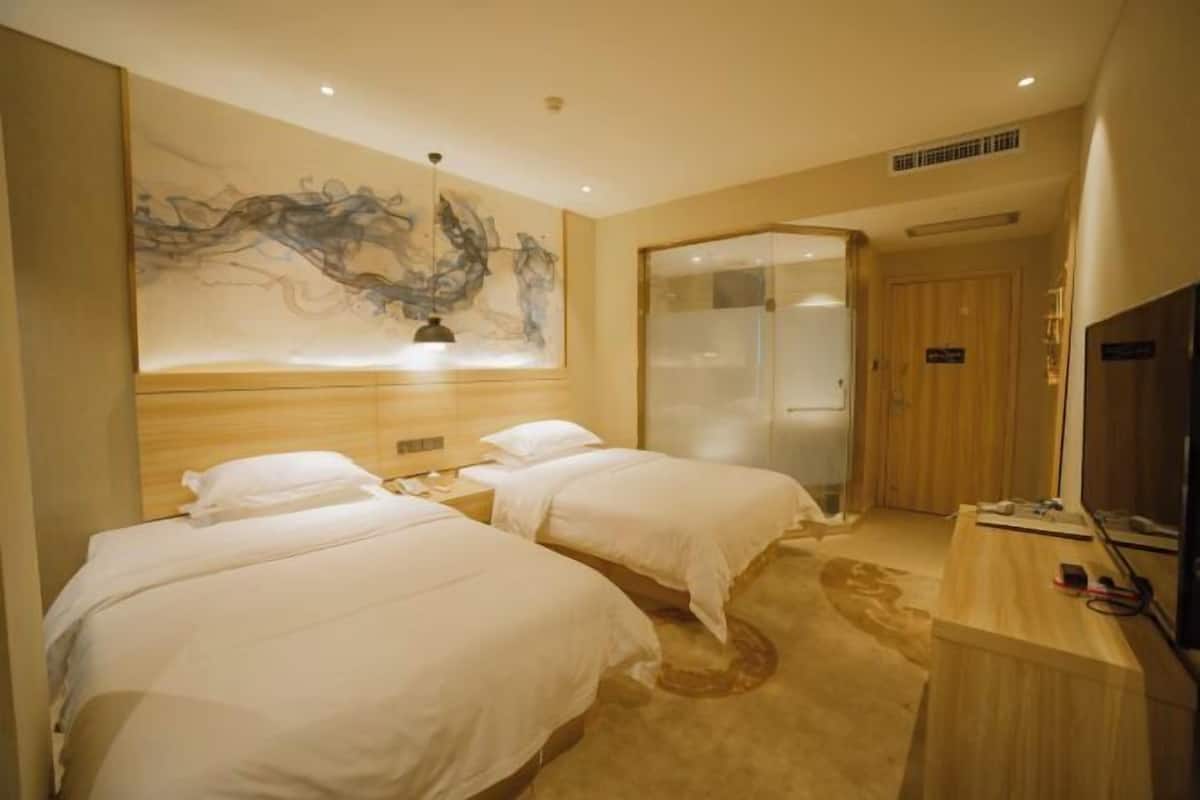 A hotel room with two beds, a large abstract painting on the wall, a wooden desk, and a television.