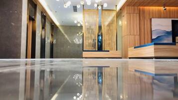 A hotel lobby with a reflective floor, wooden reception desk, and a modern chandelier.