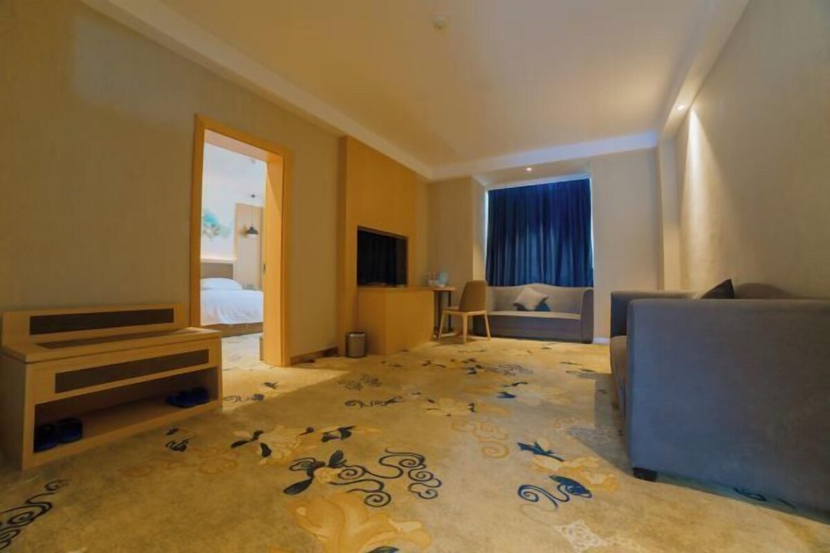 A hotel room with a bed, a sofa, a desk, and a patterned carpet.