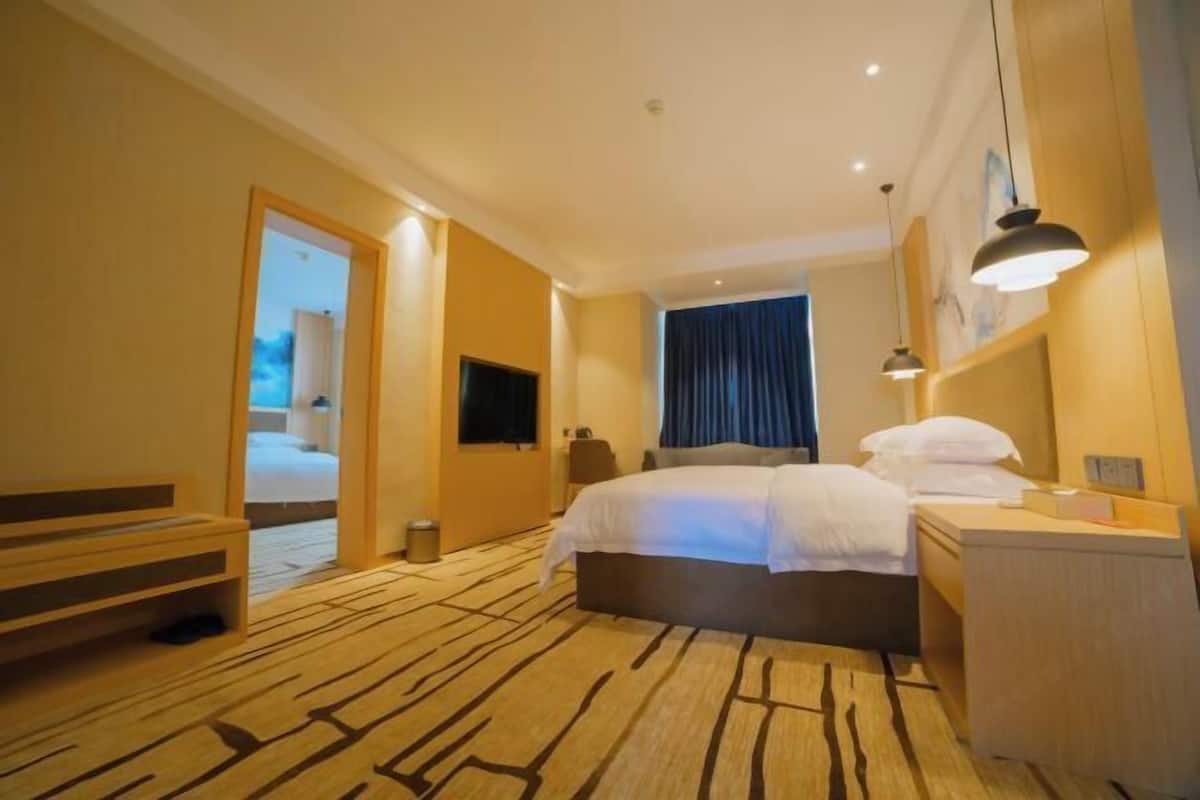 A hotel room with a bed, bedside table, lamp, and a view of the outside.