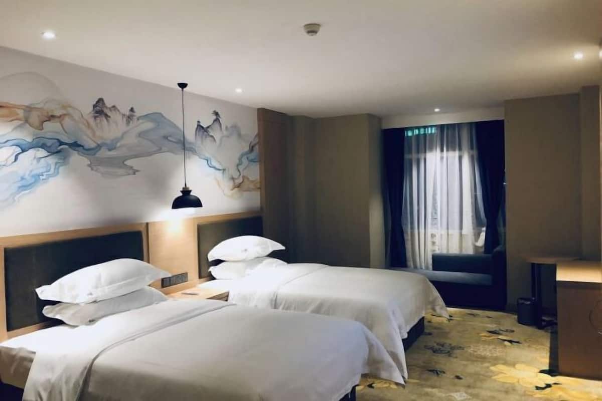 A hotel room with two beds, a large wall mural, a window with curtains, and a desk with a lamp.