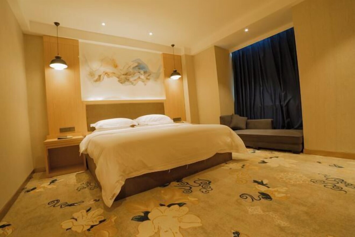 A hotel room with a large bed, a nightstand, a sofa, and a wall-mounted artwork.